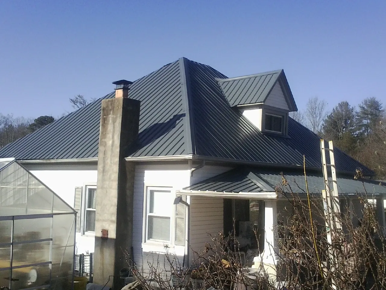 Dark blue standing seam metal roof on a white farmhouse with dormer — Slate & Tile Roof Repair by Roofing Brothers in Merion Station