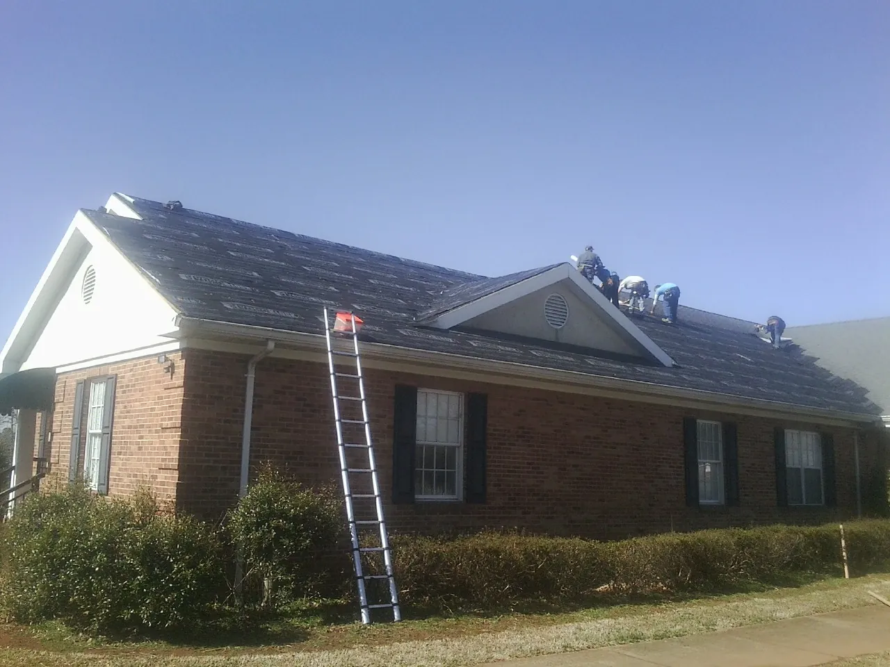 Crew tearing shingles off a brick ranch roof with a ladder set — Metal Roof Repair work by our crew in Merion Station
