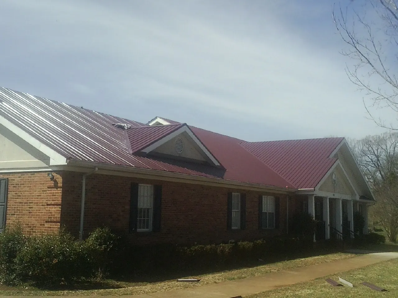 Red metal roof with gabled entries on a long brick building, from a Hail Damage Roof Repair job in Merion Station