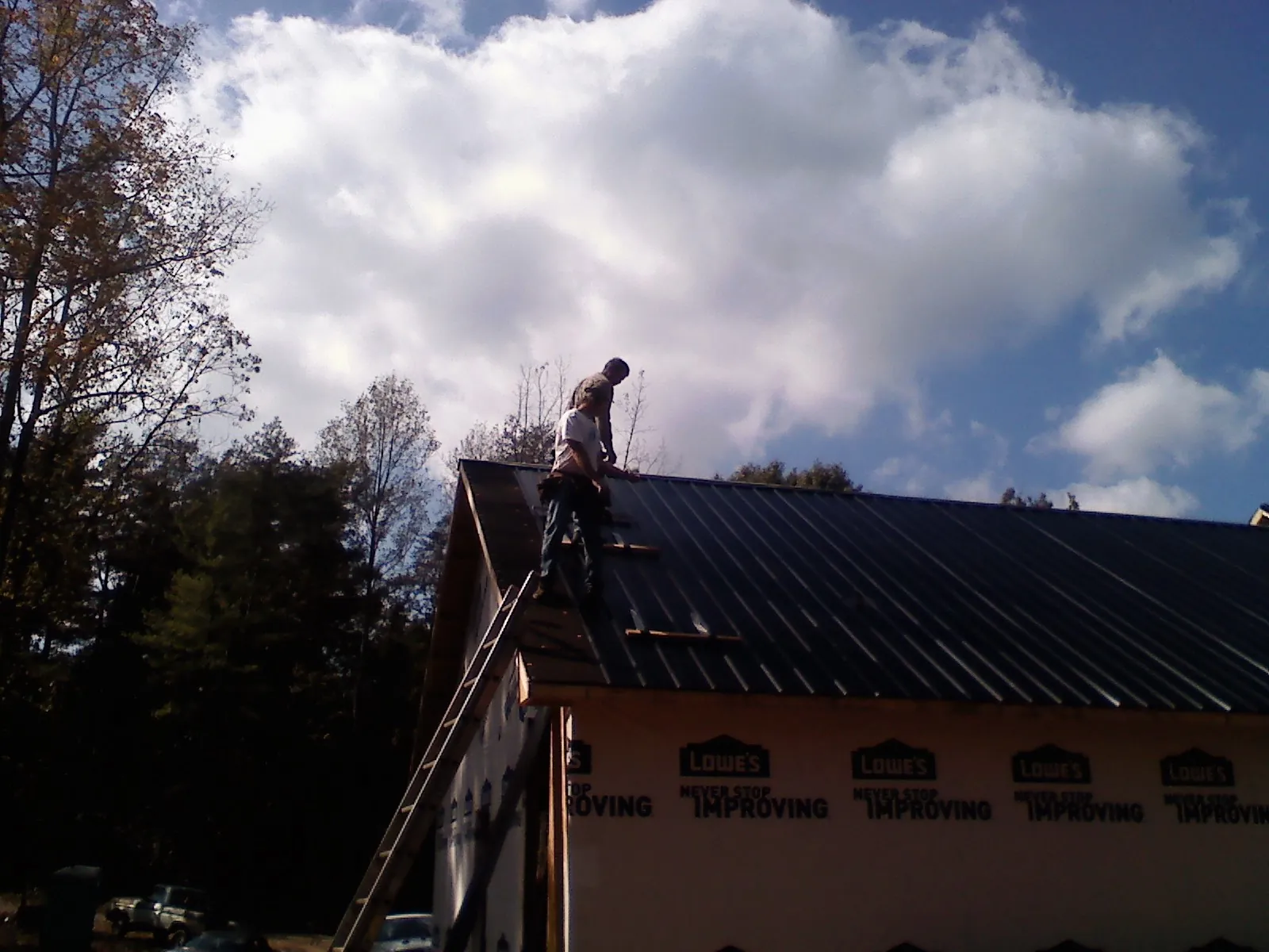 Roofer fastening dark metal panels high against a cloudy sky, from a Roof Inspection job in Merion Station