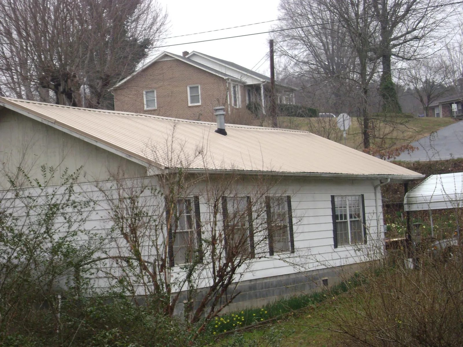 Tan metal roof on a white sided house set into a hillside — Commercial Roofing by Roofing Brothers in Merion Station
